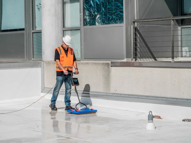 Operator pushing a Detec low-voltage scanning platform across a wetted roof membrane