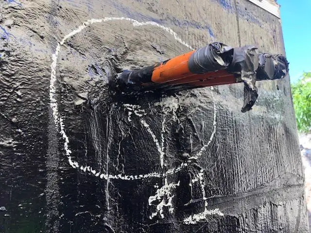Pipe penetration through a bituminous basement wall membrane, with the breach circled in chalk